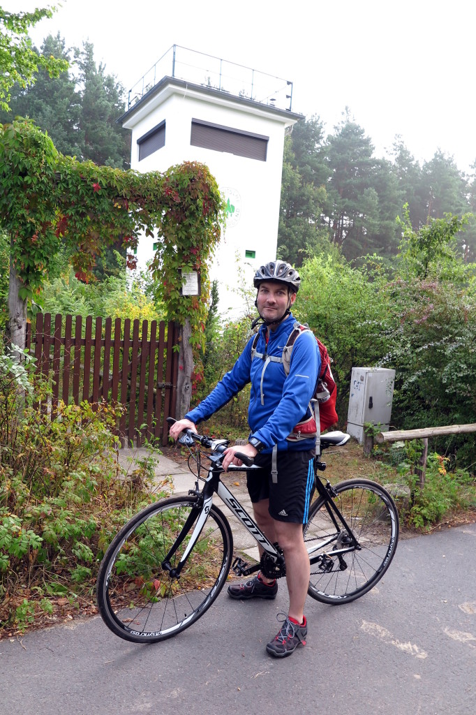 Me (Ryan Hellyer) standing on my bike, in front of a guard tower on the Berlin Wall route